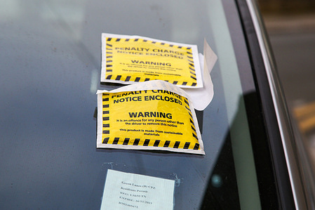 Two parking fines and penalty charge notices were displayed on a windscreen of a car parked illegally on a street.