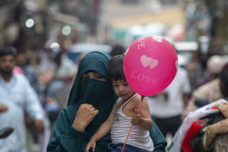 Kashmiri hijab-clad woman holds her child as she walks at a marketplace during hot summer day in the summer capital.