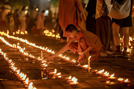 A Buddhist novice monk lights traditional Lanna oil lamps in front of the stupa at Wat Chedi Luang during National Mother's Day celebrations in Chiang Mai.