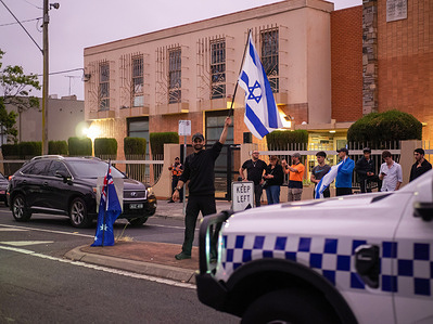 Flags and police are seen outside the Caulfield Hebrew Congregation. Pro-Palestine activists canceled plans to protest an Israeli panel event at Caulfield Hebrew Congregation after online threats emerged. Hundreds of pro-Israel supporters gathered outside in solidarity with the event, while police escorted a small group of pro-Palestine activists who attended. Two individuals were arrested.