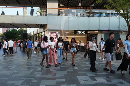 Shoppers walk through the Sanlitun outdoor plaza, with the Dior store visible in the background, Beijing.