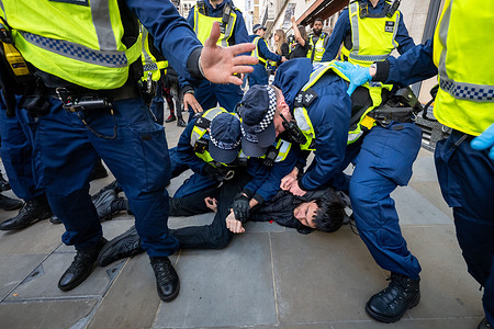 A protester is being held on the ground during a police arrest. Animal rights activists stage a protest outside a Louis Vuitton store on Bond Street, blocking the entrance and making loud noises to disrupt business and deter shoppers from entering. The demonstration, organised by campaigners opposing the use of animal furs in fashion, calls on luxury brands such as Louis Vuitton to end the use of fur.