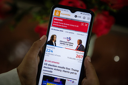 In this photo illustration, a girl holds a smartphone showing the Aljazeera English television website as she awaits the 2024 US election vote count between Donald Trump and Kamala Harris in Srinagar, India. American voters have gone to the polls to determine the 47th president of the United States. Polling over recent weeks has indicated a tight race between Democratic presidential nominee, Vice President Kamala Harris, and Republican presidential nominee, former President Donald Trump, to succeed President Joe Biden in the White House.