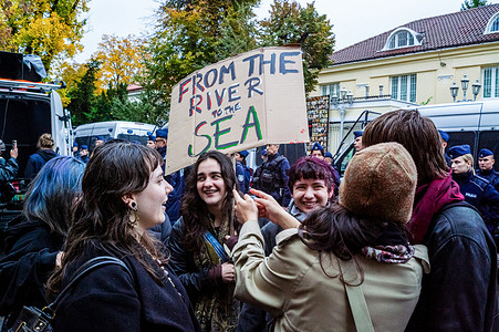 Protesters meet and talk while holding a placard that says "From the river to the sea". Pro-Palestinian demonstrators gathered to march through the streets from the De Gaulle roundabout to the Israeli Embassy. Despite the fragile ceasefire, the protesters express their anger at the two-year genocide of the Palestinian people and demand justice.
