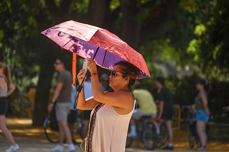 A woman seen photographing the monumental waterfall in Ciutadella Park protecting herself from the sun with an umbrella. The city is experiencing its first heat wave of the year with temperatures reaching 34 degrees Celsius, an unusual temperature for June. The heat wave is expected to last until Wednesday.