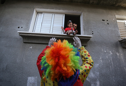 A palestinian youth dressed as a clown while wearing a protective gloves and a mask, staged a street performance to entertain children trapped at home due to the Corona Virus outbreak in Khan Yunis, southern Gaza Strip.