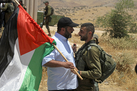 An Israeli soldier suppresses a Palestinian Protester holding a Palestinian flag during the demonstration against land confiscation in the northern Jordan Valley in the occupied West Bank.