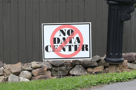 A “No Data Center” yard sign is displayed in front of a house in opposition to a proposed 300-megawatt data center at the nearby Great Stream Commons industrial park. Local residents in Union County, Pennsylvania, protest against PNK Group's proposed data center at Great Stream Commons, citing concerns over its potential impact on the local power grid, water supply, property values, and noise generated by the facility's cooling infrastructure.