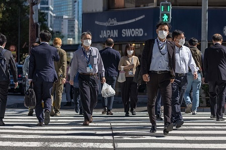 People wearing masks walk across a street in the business district Toranomon Hills in Tokyo.