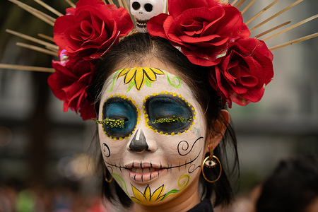 A woman with a brightly colored Catrina face paint poses for the camera during the Catrina Festival. Thousands of people took to the streets of Mexico City to watch the procession of Catrinas. Catrina is a female skeleton with a large hat, often made of feathers. The figure is based on a character created in the early 1900s by artist José Guadalupe Posada and then reinvented by Diego Rivera.