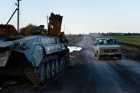 A vehicle with the sign '+' markings, often found on Ukrainian army vehicles, is driving past a destroyed tank with the symbol 'Z', markings often found on Russian military vehicles near the border of Kharkiv and Donetsk region. The fight between Ukraine and Russia intensifies as Ukrainian troops continue their advancement near the border of Luhansk, Donetsk, and Kharkiv region. Many settlements have become abandoned after residents escaped due to the fight. The liberation of Lyman and Zelena Dolyna, strategic cities in the Donetsk region, was a symbolic victory for Ukraine.