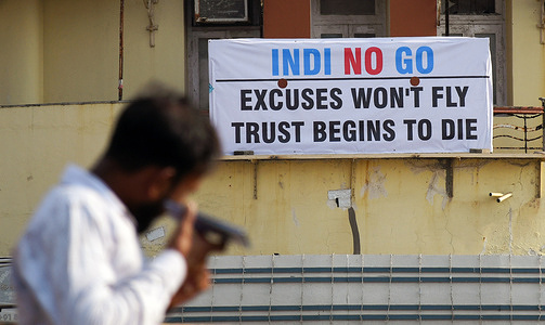 A man talks on his mobile phone near the poster placed above a restaurant criticising Indigo Airlines in Mumbai. IndiGo, the country’s largest airline, cancelled flights nationwide due to a pilot shortage after failing to plan for new duty-hour regulations, leaving passengers stranded at airports. Many frustrated travelers waited for hours without clarity on rescheduled flights or alternative arrangements, leading to arguments with ground staff as people demanded refunds. The widespread cancellations caused heavy crowding at airports and forced many passengers to miss both personal and professional commitments.
