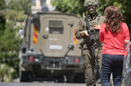 An Israeli soldier seen preventing a Palestinian woman from crossing the street during a military operation targeting the Rafidia neighborhood in the West Bank city. Israeli forces raided Palestinian shops and homes and closed off the area surrounding An-Najah National University. Residents reported that the army arrested a Palestinian man during the operation.
