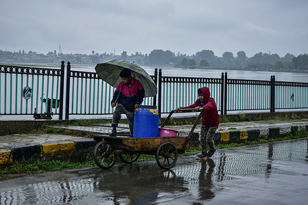 A boy pushes a cart while other holds an umbrella during rainfall in Srinagar. Rainy weather continued in Kashmir for the sixth straight day on Tuesday while the weatherman has predicted significant improvement in prevailing weather conditions from Wednesday onwards.