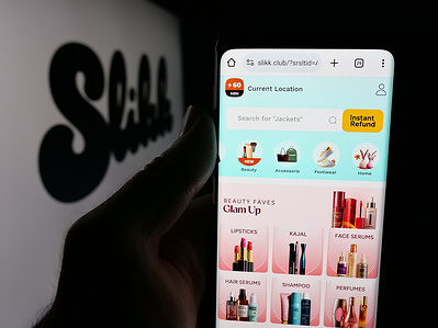 In this photo illustration, a person is holding a cellphone with the webpage of Indian fashion marketplace company Slikk on screen in front of logo.