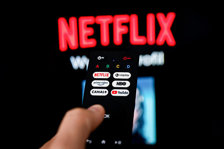 In this photo illustration a Netflix logo seen on a TV remote in front of the TV.