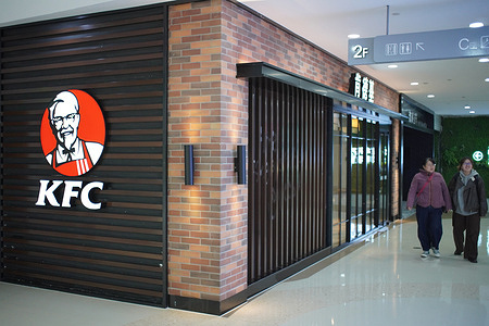 Two women walk past the brick-and-metal facade of a KFC restaurant at the Wuyue mall.