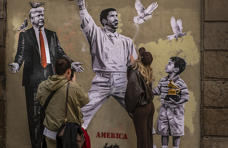 A young woman poses for a photograph in front of Alberto Leon's mural depicting singer Bad Bunny in contrast to the political leadership of President Donald Trump; she is seen on a street near the post office area. In an alley in the historic center of Barcelona, ​​the artist Alberto Leon has created a mural depicting the singer Bad Bunny in contrast to the political leadership of President Donald Trump.