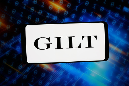 In this photo illustration, the logo of US e-commerce company Gilt Groupe is displayed on a smartphone in front of abstract background on computer screen.