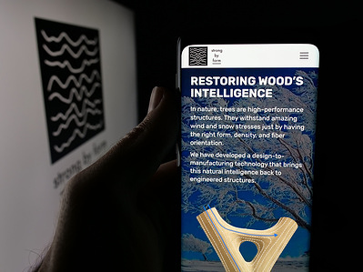 In this photo illustration, a person is holding a smartphone with the web page of Chilean materials company Strong by Form on screen in front of logo.