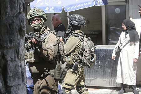 An Israeli soldier aims his weapon and takes up position while escorting an Israeli intelligence officer in the commercial market under heavy guard. This operation drew attention of shoppers in the market amidst heavy security presence accompanied by the officers' movements in the commercial area.