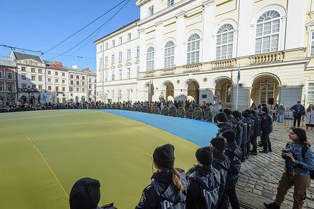 Military personnel, cadets and policemen sing the national anthem while holding a huge Ukrainian flag in front of the city hall Ratusha in honor of the anniversary of the first performance of the national anthem 158 years ago.