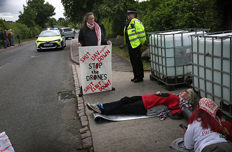 A supporter holds a banner saying ’Shut UAV down’ with other activists seen laying in a lock-on device outside the factory. Four activists from People Against Genocide shut down the UAV Engines factory by locking themselves outside the only two entrance gates. The company, a subsidiary of Israeli arms manufacturer Elbit Systems produces engines for drones the activists say are used against Palestinians and other targets in the Middle East. The protesters are calling for Elbit Systems to get out of the UK.
