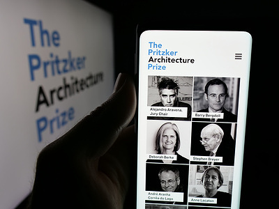 In this photo illustration, a person is holding a smartphone with the webpage of award Pritzker Architecture Prize on screen in front of logo.