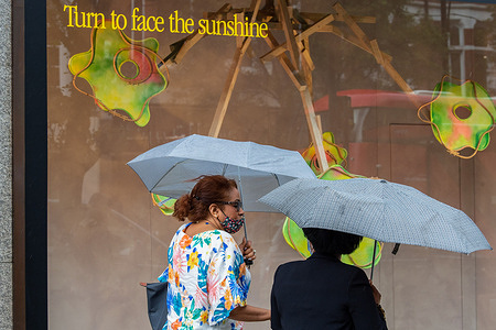People protect themselves from rain under umbrellas as they walk by a sign in a shop window reading, Turn to face the sunshine on Oxford Street