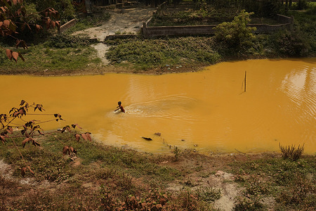 A child seen playing in a canal which is polluted by wastewater from a Water treatment plant at Savar in Dhaka.
In 2019 Bangladesh government opened a Water Treatment Plant/ Iron Removal Plant by Dhaka WASA (Water and Sewerage Authority). But this treatment plant throwing waste directly into the surrounding canal. The water colour of one of the local water sources turns into yellow. Local people complain that when they take a bath here, their bodies itch and their clothes change colour. Moreover, the colour of the soil has changed.