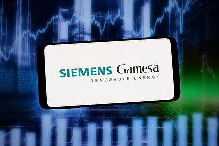 In this photo illustration, the logo of company Siemens Gamesa Renewable Energy is displayed on a smartphone in front of abstract background on computer screen.