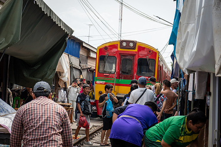 A view of vendors and tourists returning to normal after the train has just passed at the Maeklong Railway Market in Samut Songkhram, Thailand. The Maeklong Railway Market, commonly called Siang Tai (life-risking) Market is a busy local market and popular tourist spot in Samut Songkhram Province, in Thailand. Trains pass through several times daily, and vendors quickly pull back their umbrellas and displays just before the train arrives, then return everything afterward. The market sells fresh produce, seafood, snacks, clothing, and souvenirs like any traditional Thai market.