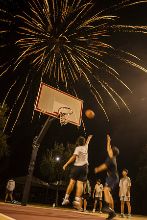 People play basketball amid fireworks under the night sky above the basketball courts at Rosemead Park during Fourth of July celebrations.