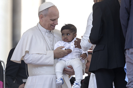 Pope Leo XIV carries a child during his weekly general audience in St. Peter's square at the Vatican.