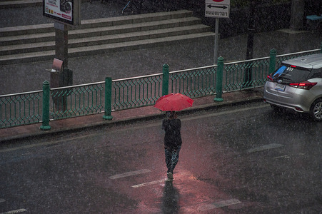 A person walks across Ratchadamri Road while holding an umbrella on a rainy day.