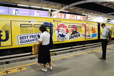 A BTS Skytrain decorated with Japan, Thailand and Hong-Kong stickers from an Expedia advertisement passing through as passenger wait for the next train in Bangkok.