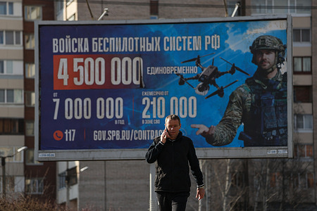 A man walks past an outdoor advertising billboard with the slogan "Irreplaceable" and information about recruitment for the unmanned systems units of the Russian Armed Forces, installed on a street in St. Petersburg. Outdoor advertising across St. Petersburg encourages citizens to enlist in the Russian Armed Forces under contract. Some billboards focus on recruitment for new units such as the Unmanned Systems Troops, highlighting opportunities for specialized training lasting at least three months. The campaign emphasizes technological roles and operator training as part of expanding new military branches. The advertisements are integrated into the urban environment, including near residential areas and public facilities.