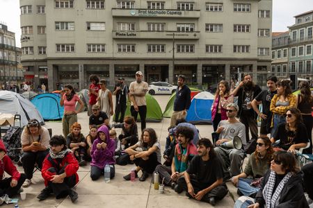 Participants have a public assembly beside a temporary encampment in Praça D. João I during an overnight occupation organized by the “Não Dá Mais Para Viver Assim” movement following demonstrations against the housing crisis and rising living costs.