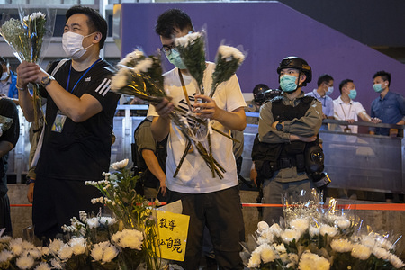 People lay flowers under police surveillance at the entrance of Prince Edward MTR railway station commemorating the tenth month after hundreds of anti-government demonstrators were attacked by riot police in clashes at the subway station.
