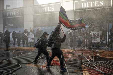 A man holds a Mapuche flag as a group of protesters confront riot police during the demonstration.
Protesters gathered near the former national congress during the first day of the constitutional convention.