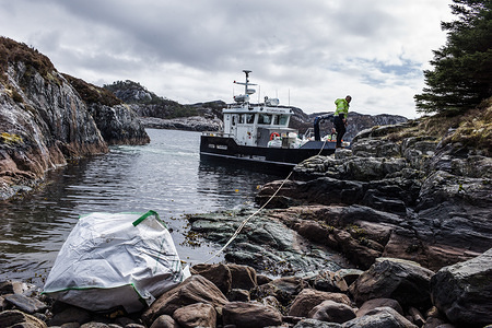 A boat operator seen hauling a large bag of plastic waste which has been collected during the beach cleaning event.
Around 150 volunteers from 12 countries attended the Plastic Whale Heritage beach cleaning event in Norway. The event took place in 6 bays on the islands off the coast of Sotra.