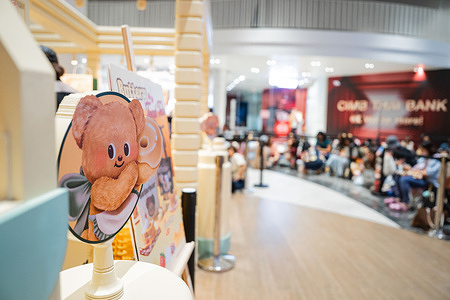 A Butterbear display panel stands prominently at Buttery World, with a crowd of fans in the background drawn to the viral Thai mascot. Butterbear mania takes over Siam Paragon in Bangkok as fans gather around the viral Thai mascot-turned-internet idol during a public appearance at her pastry shop. Known as “Nong Noey,” she has evolved from brand mascot to pop culture icon, with dance covers, reaction videos, and music clips. Once a hit among Chinese tourists, Butterbear now charms fans worldwide.