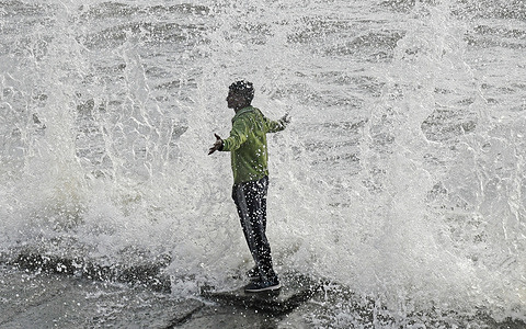 A man enjoys as waves crash against the shore during high tide at a beach. People came to the beach to enjoy the dry weather after experiencing a week of extremely heavy rain, which brought the city to a standstill, flooding the streets with water, causing traffic on the roads, delaying the trains due to flooded tracks, school and colleges to remain closed, affecting attendance in the offices across the city.