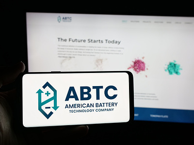 In this photo illustration, a person is holding a smartphone with the logo of American Battery Technology Company (ABTC) on screen in front of website.