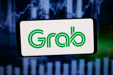 In this photo illustration, the logo of Singaporean app company Grab Holdings Inc. is displayed on a smartphone in front of abstract background on computer screen.