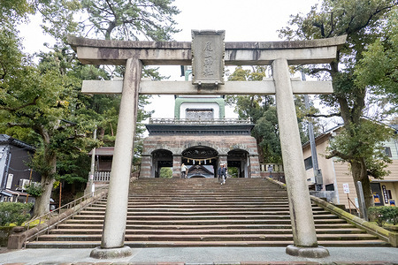 The stone torii gate and staircase leading to Oyama Shrine seen with visitors walking through the historic shrine entrance. Oyama Shrine in Kanazawa is a Shinto shrine known for its unique gate that blends Japanese, Chinese, and Western architectural elements. Dedicated to Maeda Toshiie, a powerful feudal lord, it sits near Kanazawa Castle and features tranquil gardens and ponds.