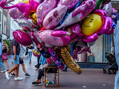 People walk past a woman selling balloons along the street. The Vierdaagsefeesten (Four Days Festivities) is a seven-day citywide festival held annually in Nijmegen, Netherlands, alongside the International Four Days Marches, the world's largest walking event. Established in 1970, the festival celebrates the tens of thousands of international participants with free live music, theater, food markets, and cultural events across more than 40 stages, attracting over 1.5 million visitors each year.