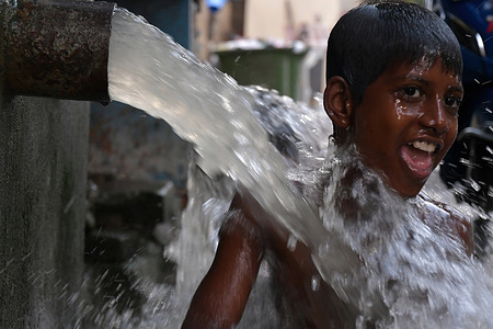 A boy is bathing at a roadside municipal tap on a hot summer day.