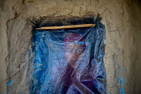 A Kashmiri girl looks out through a plastic-covered opening of her mud house on the outskirts of Srinagar, Indian-administered Kashmir.