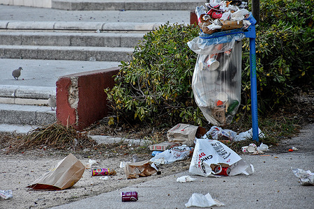 Garbage is strewn on the ground next to a full trashcan at Mistral Park in Marseille.